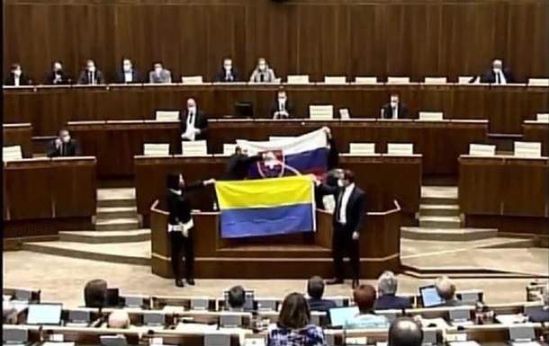 Це сталося під час обговорення оборонної угоди зі США. Одні депутати заблокували трибуну, розгорнувши словацький прапор. Інші стали поруч із прапором України.
